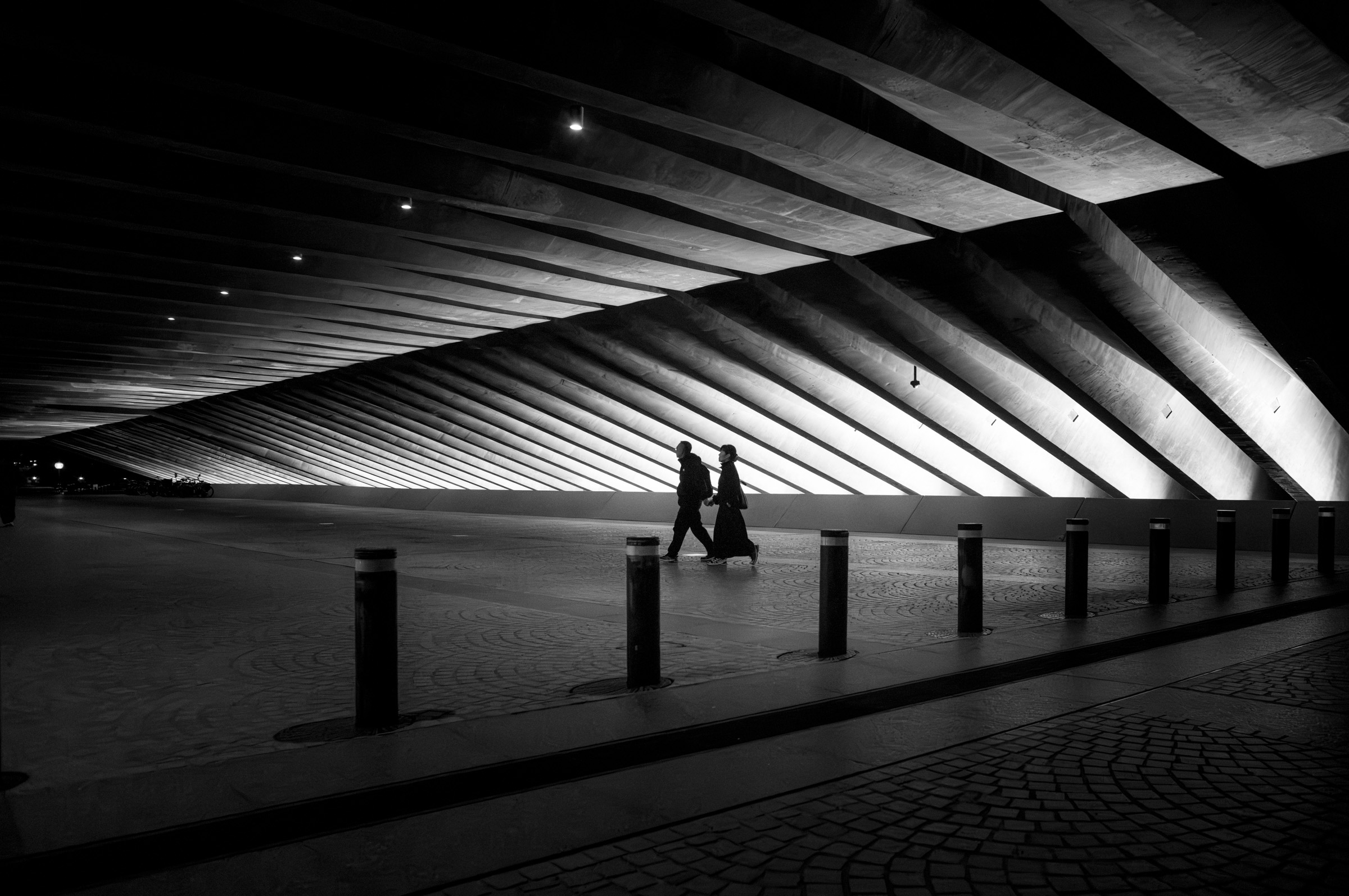 A couple silhouetted, walking under a ribbed concrete ceiling at night