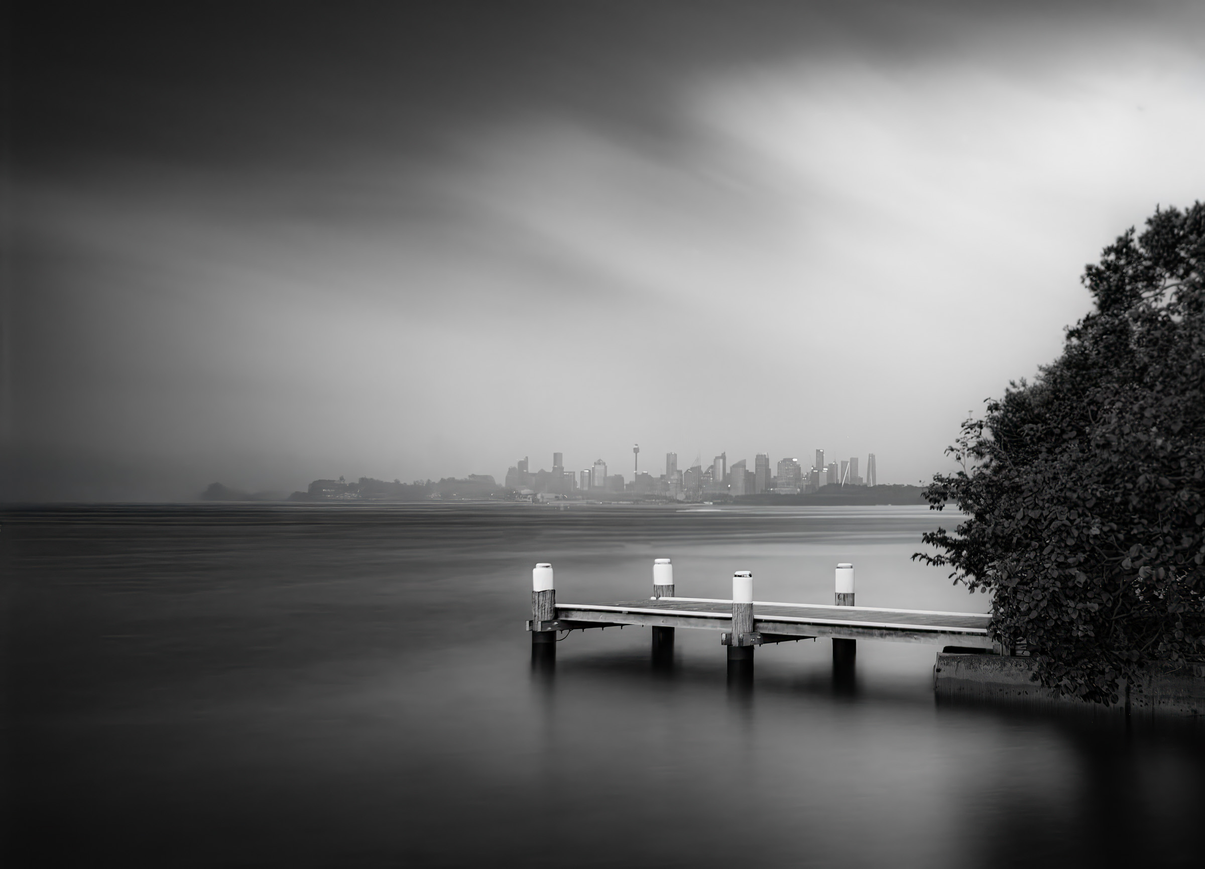 A quiet jetty and the Sydney skyline under storm light, long exposure